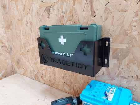Green first aid kit in a black first aid kit holder with 'TradeTidy' branding on a wooden wall
