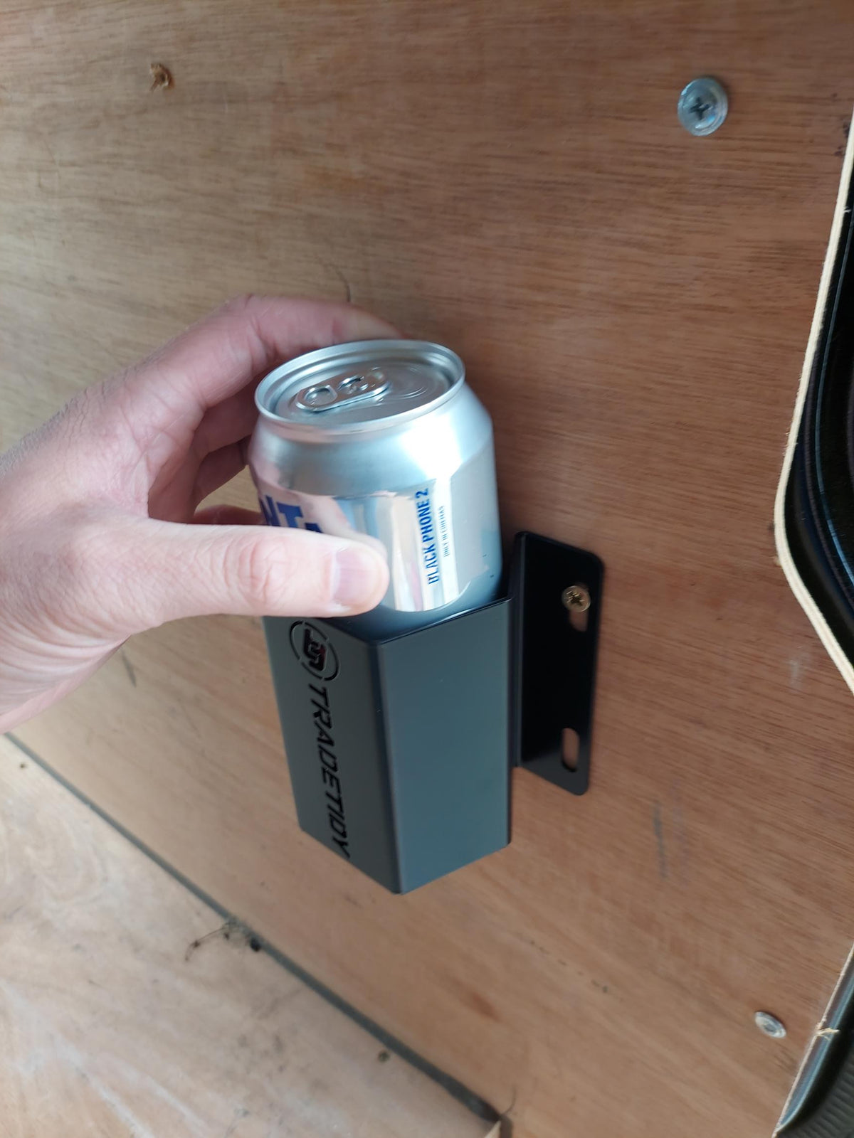 Hand holding a can in a black TradeTidy can holder on a wooden surface