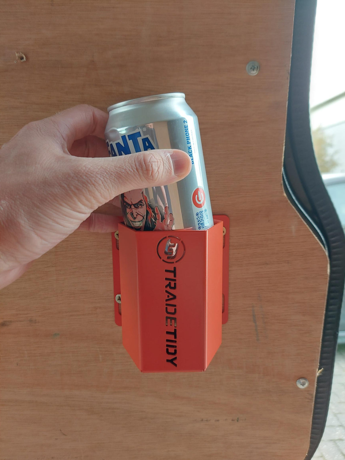 Hand holding a can next to an orange TradeTidy can holder on a wooden surface