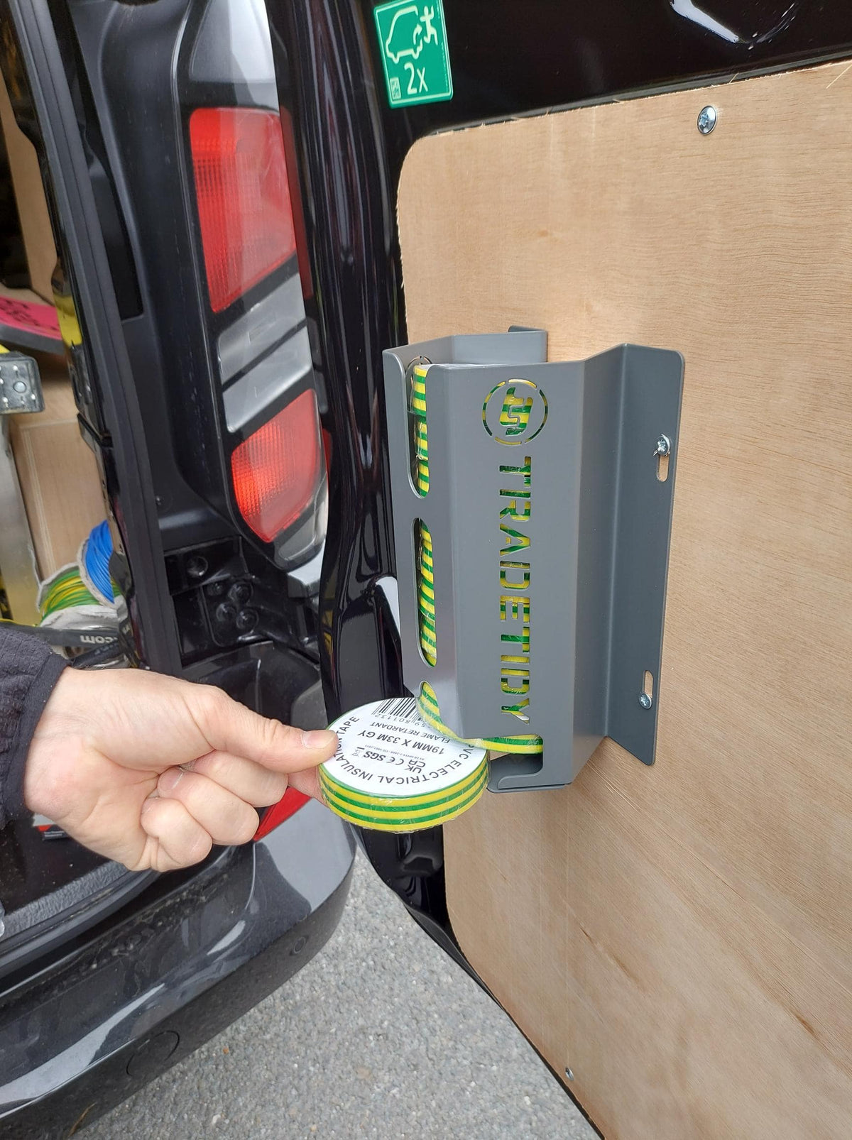Hand holding a roll of green and yellow tape next to a metal bracket with 'TradeTidy' branding.