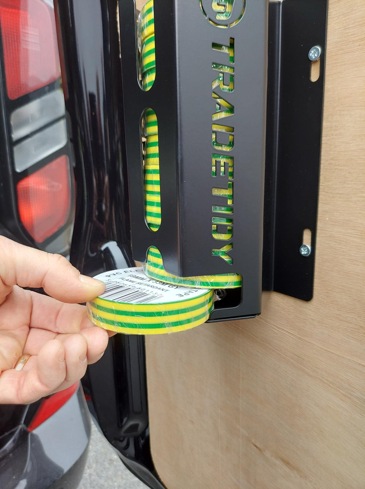 Hand holding a roll of green and yellow tape next to a metal bracket with 'TradeTidy' branding.