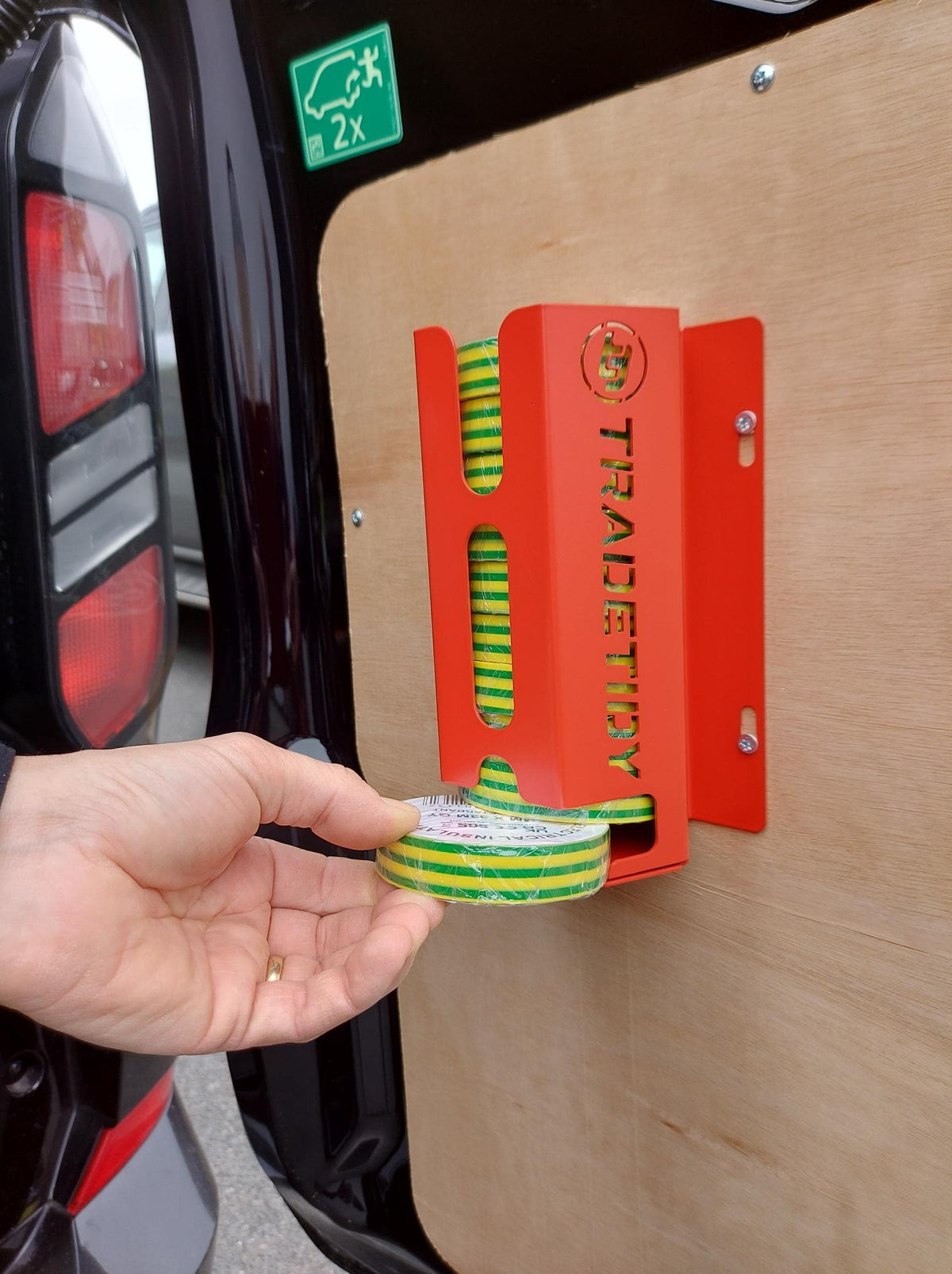 Person holding green and yellow striped tape next to a red tool with 'TradeTidy' branding on a vehicle door.