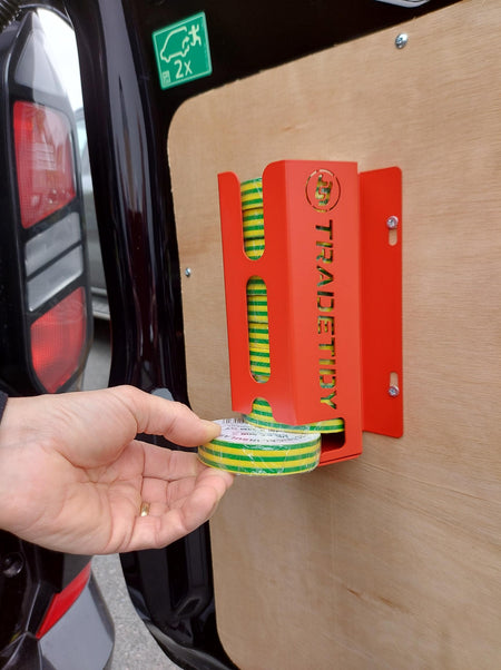Person holding green and yellow striped tape next to a red tool with 'TradeTidy' branding on a vehicle door.