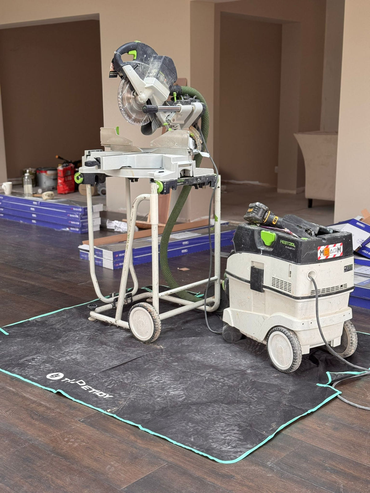 Circular saw on a stand with a carpet cleaning machine on a TradeTidy work mat in a room setting.