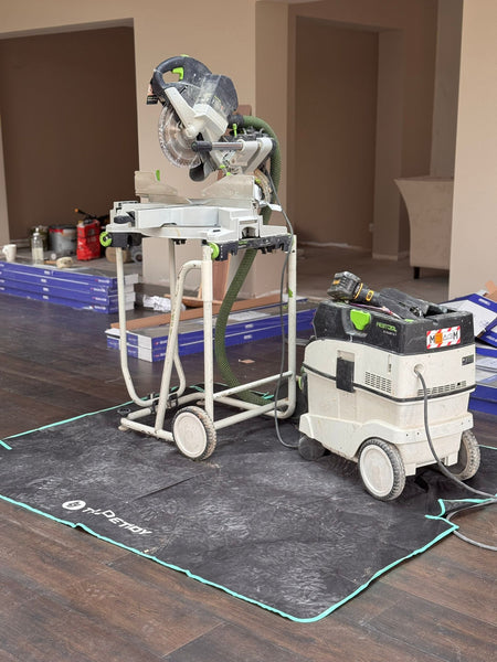 Circular saw on a stand with a carpet cleaning machine on a TradeTidy work mat in a room setting.