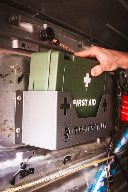 Hand placeing a Green first aid kit in a grey first aid kit holder with 'TradeTidy' branding on a workshop van's wall