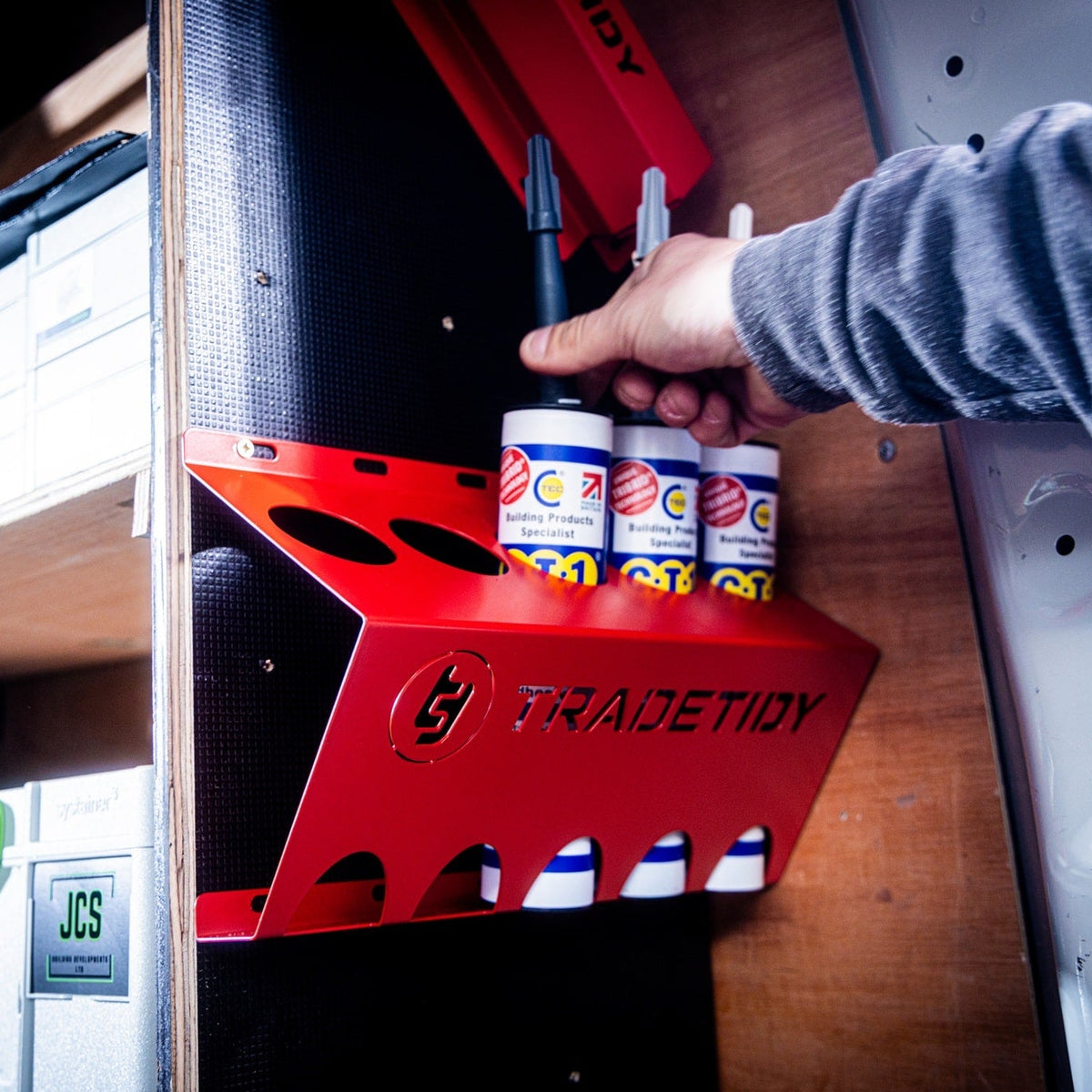 Hand holding a silicone TradeTidy tube in a red tube holder installed in a workshop van