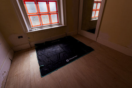 Black work mat with a tradetidylogo on a wooden floor in a room with a window.