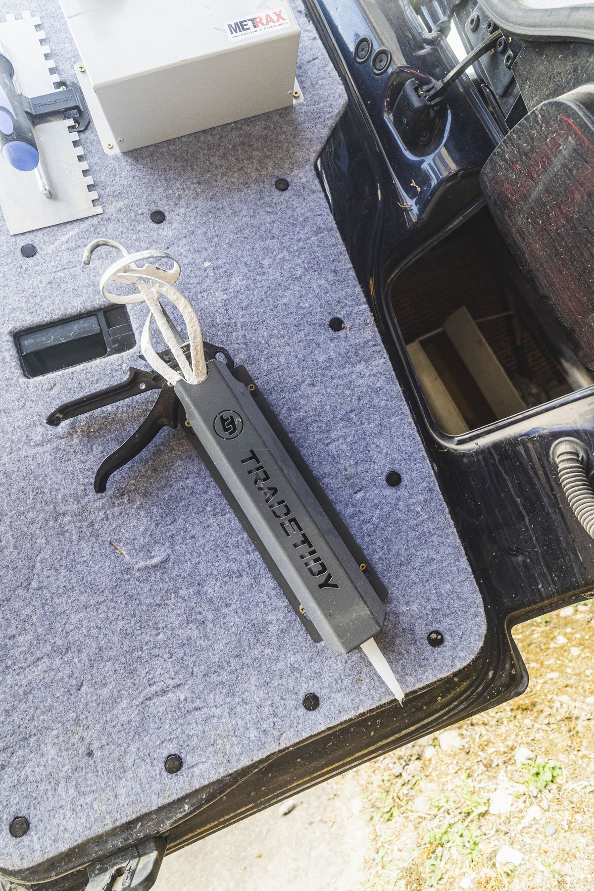 TradeTidy grey silicone and mastic gun holder on a van floor mat next to a sealant gun