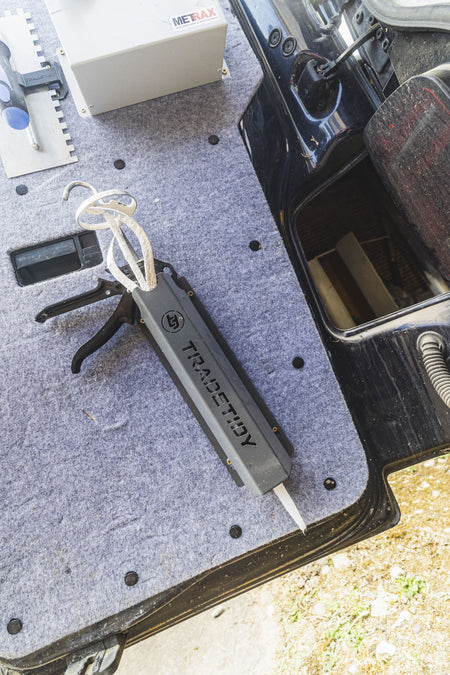 TradeTidy grey silicone and mastic gun holder on a van floor mat next to a sealant gun