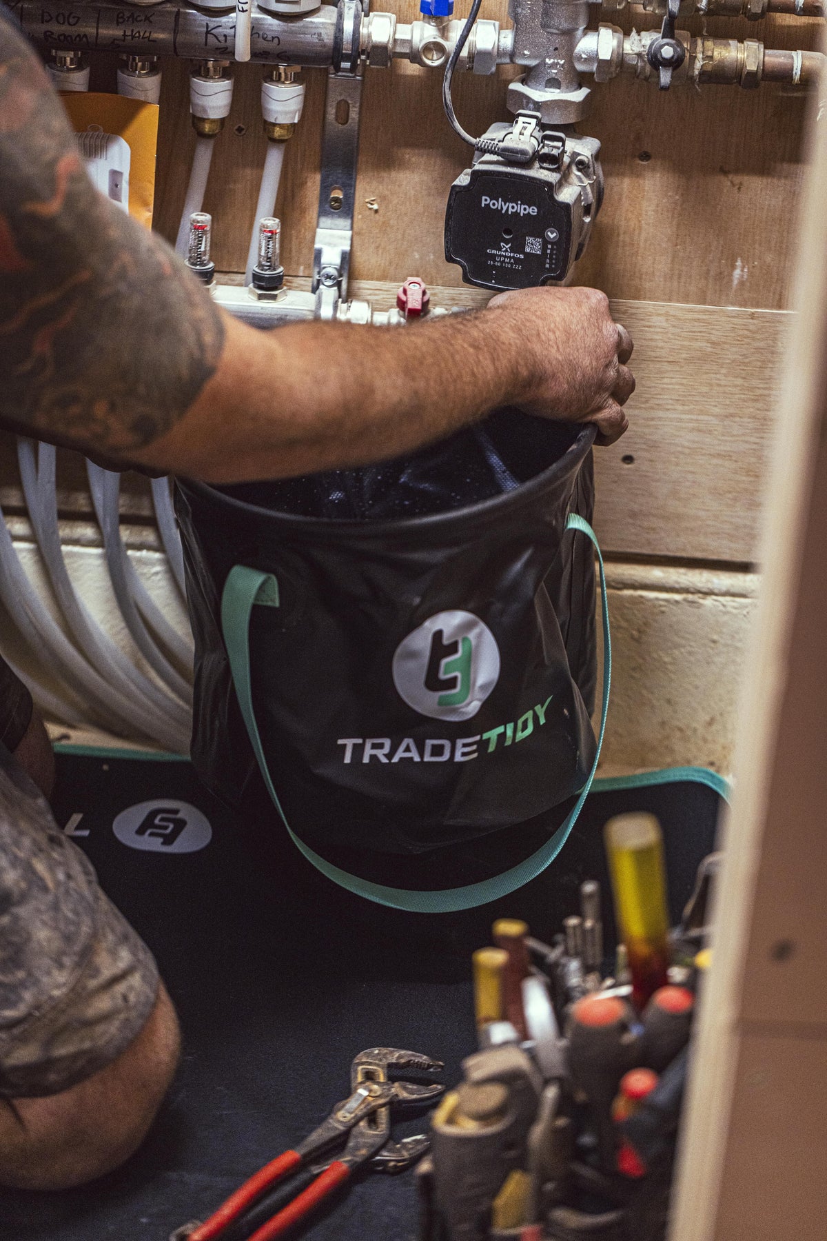 Person using a collapsible bucket with a visible TradeTidy logo in a workshop setting.