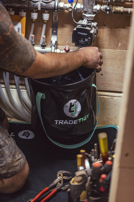 Person using a collapsible bucket with a visible TradeTidy logo in a workshop setting.