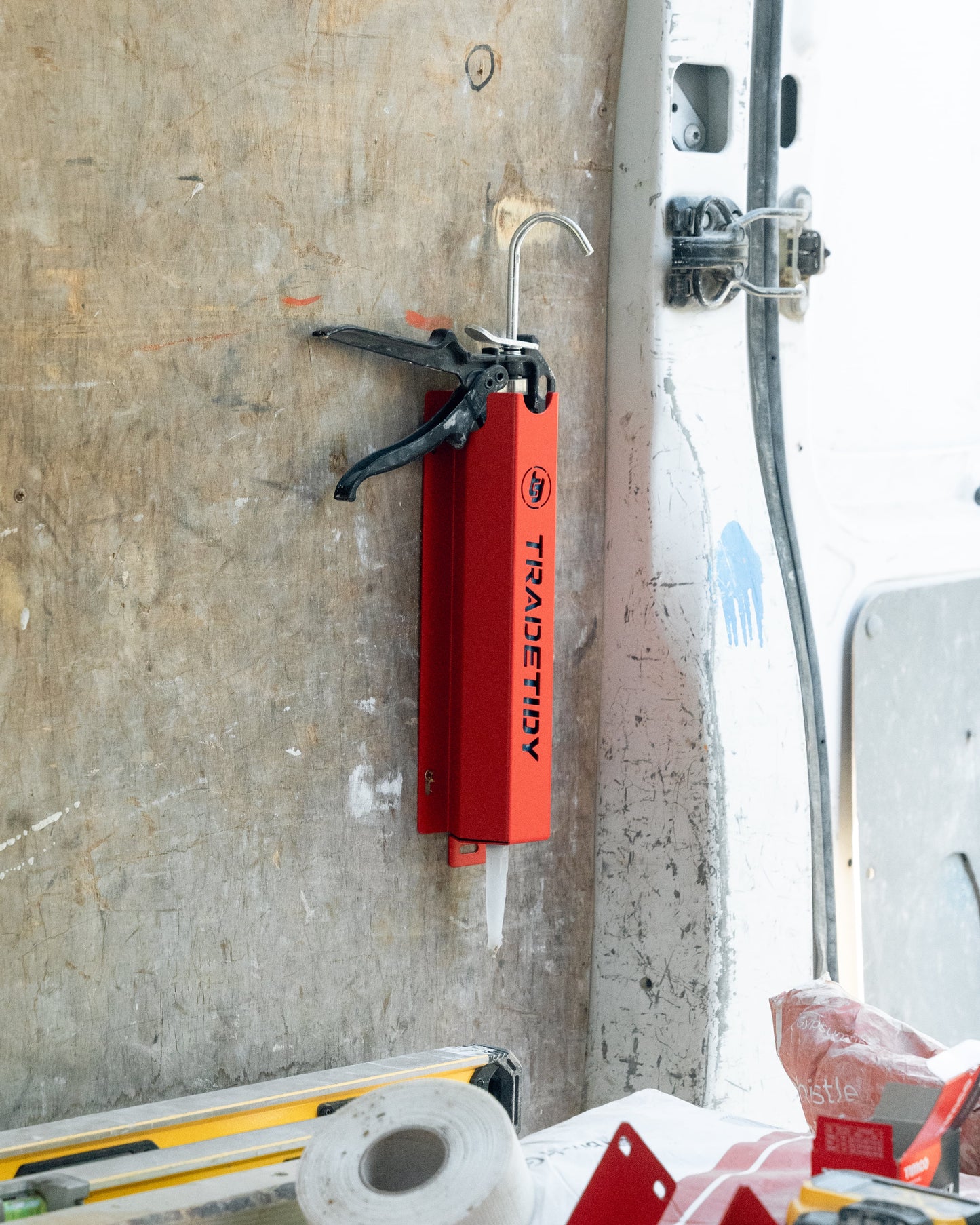 A red silicone gun holder mounted on a wall, with a silver-colored fixing lug visible.