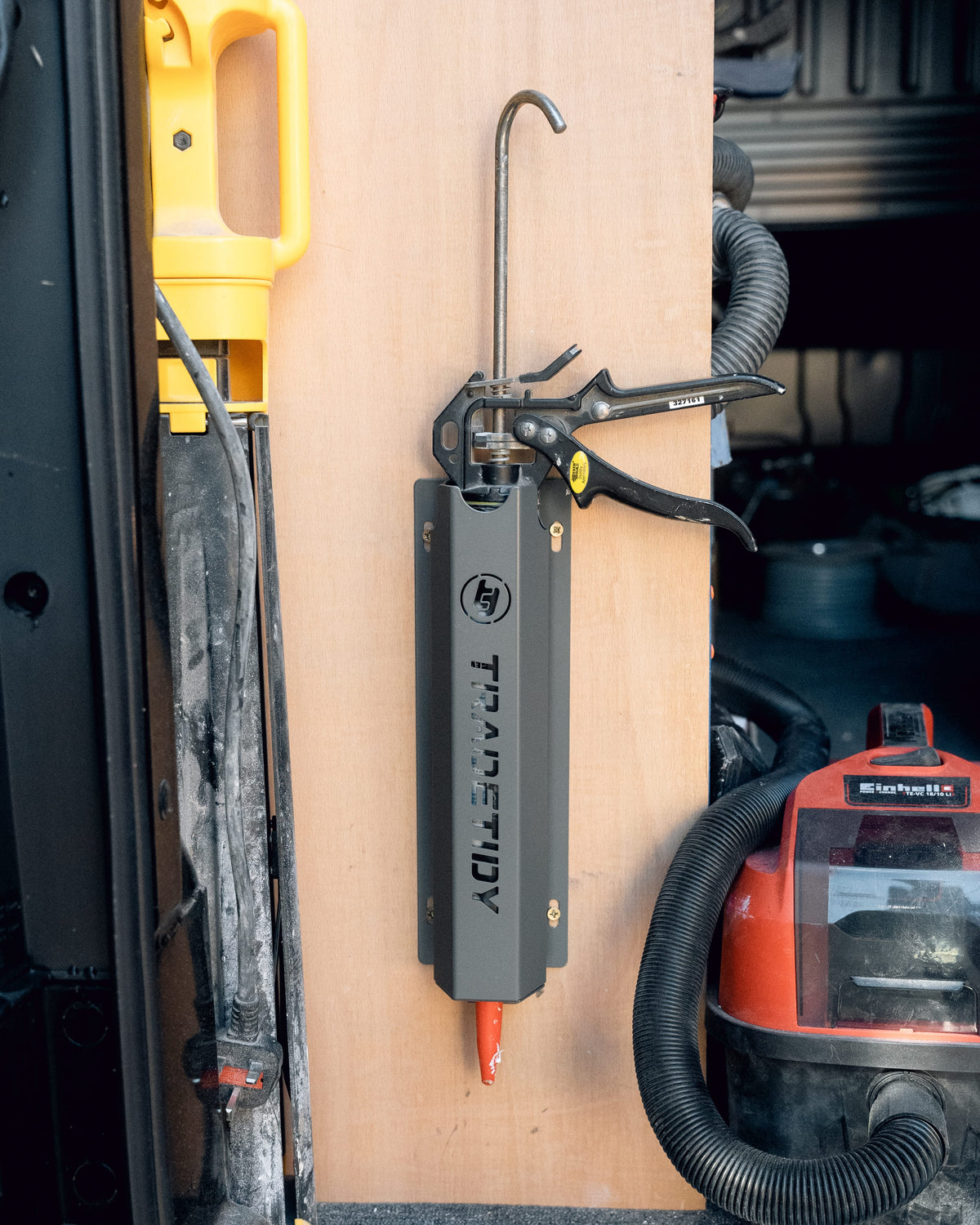 TradeTidy black silicone and mastic gun holder with a sealant gun stowed, mounted on a plywood van wall