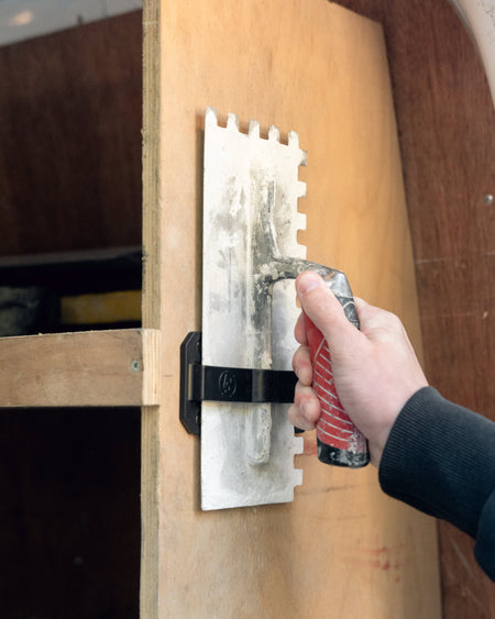 TradeTidy - hand holding and placing a trowel in a black trowel holder on a wooden wall