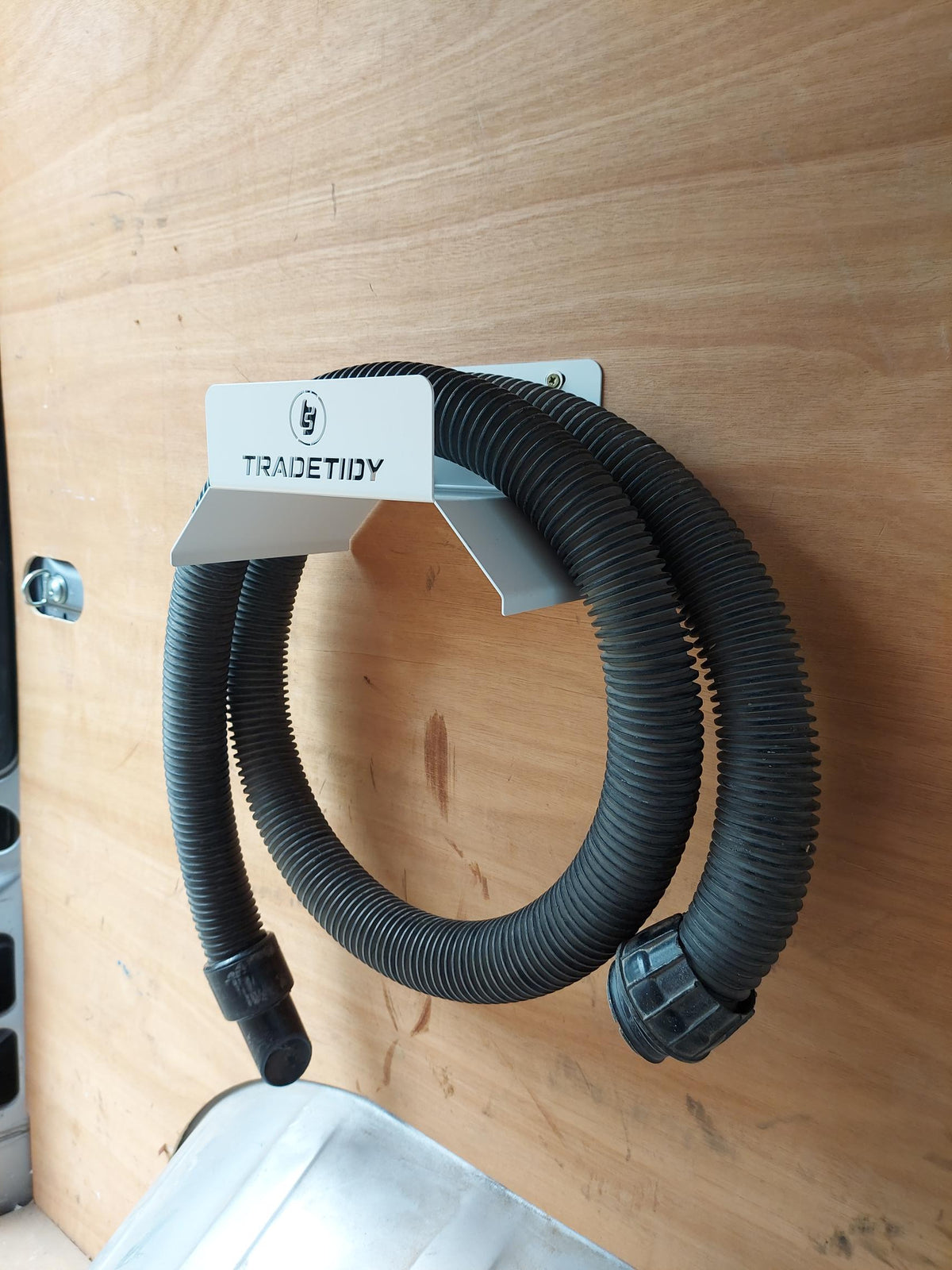 TradeTidy - Hose hanging on a white Hose Holder mounted on a wooden wall.