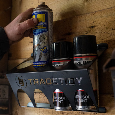 TradeTidy - Hand holding a WD-90 spray can placing it in a Black Can Holder installed on a wooden wall