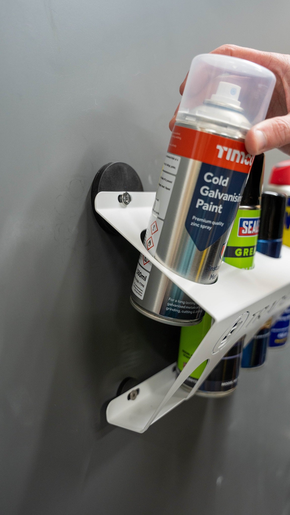 Hand holding a paint can placing it in a white metal holder mounted by a magnet TradeTidy kit on grey background